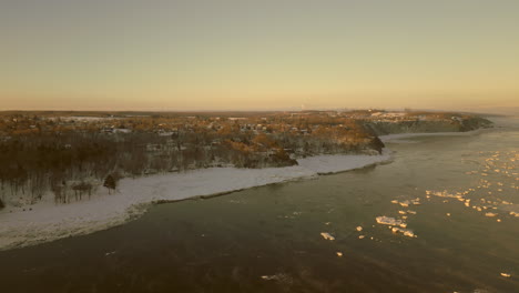 drone view going towards the coast of the canadian town of beaumont, quebec, from the st-lawrence river seaway, on a very cold winter morning