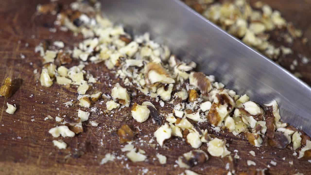 Closeup of a knife chopping nuts on a wooden table.