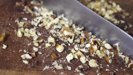 closeup of a knife chopping nuts on a wooden table.