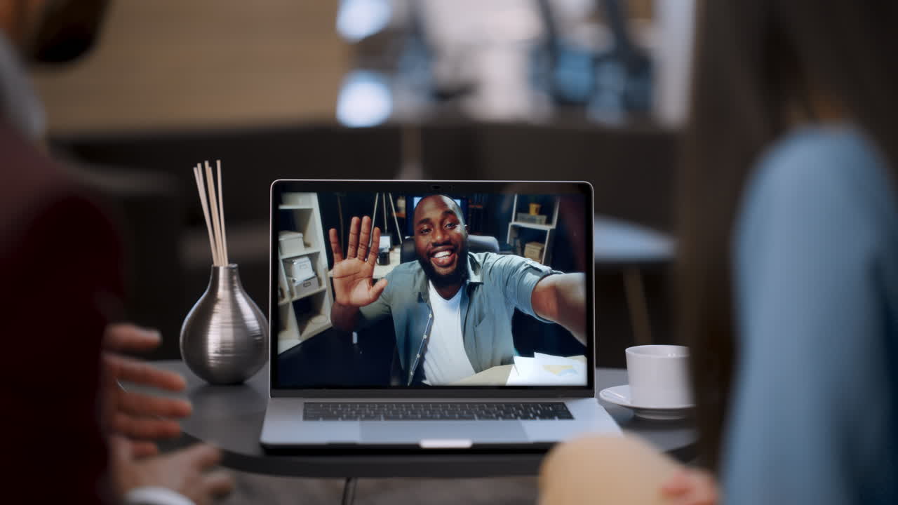 Business partners greeting video conference using laptop in cafe close up