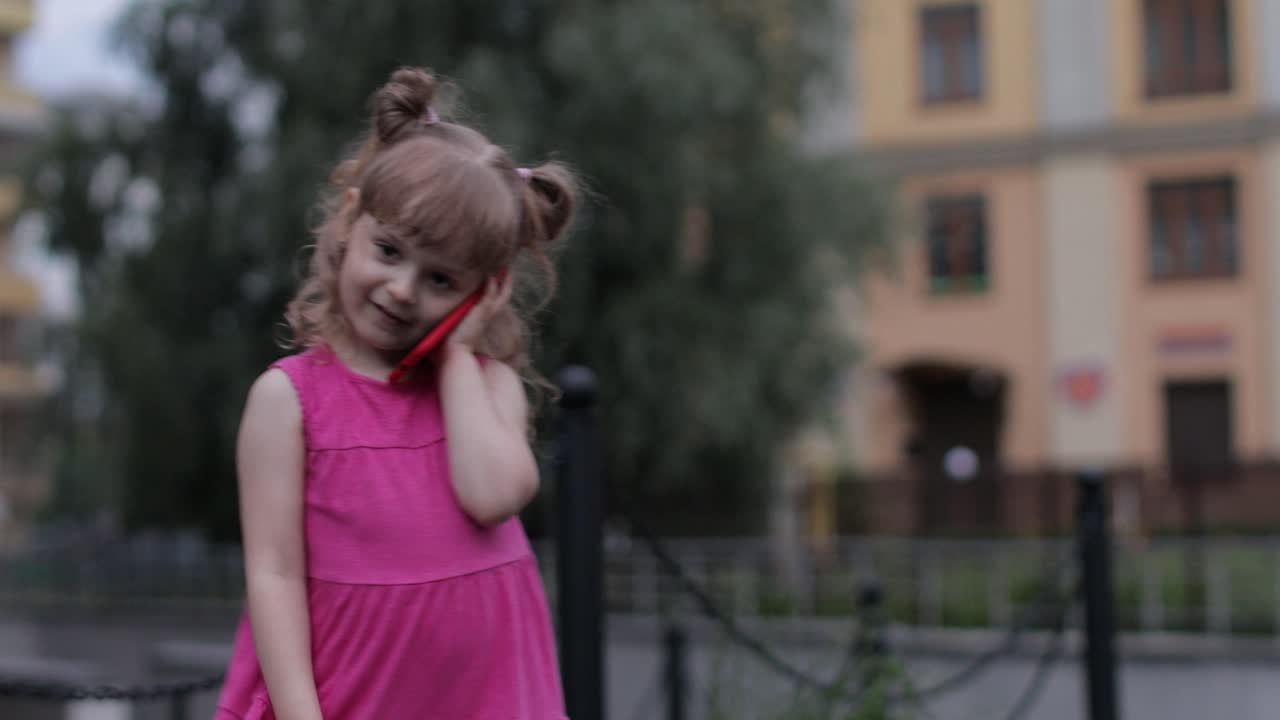 niña hablando por teléfono inteligente al aire libre. niño con vestido rosa hablando por teléfono móvil en la calle de la ciudad