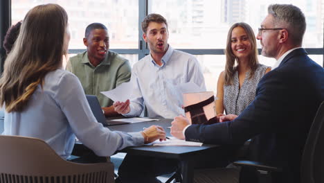 Multi-Cultural-Business-Team-Meeting-Around-Office-Boardroom-Table-With-Laptops-Discussing-Documents