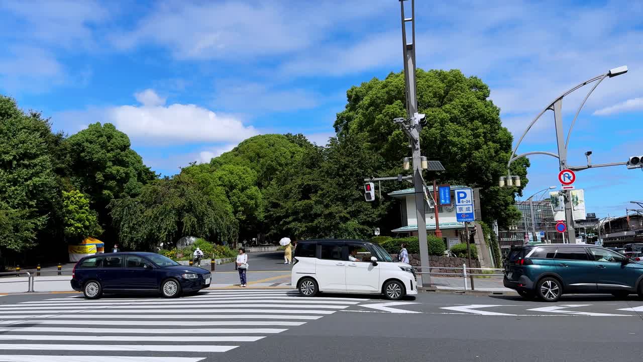 City street with cars and people crossing under a bright sky with modern buildings and greenery