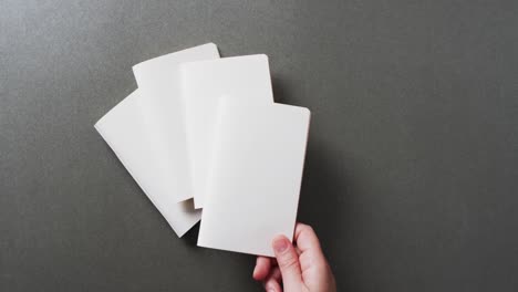 hand holding piece of paper over pieces of paper with copy space on gray background in slow motion