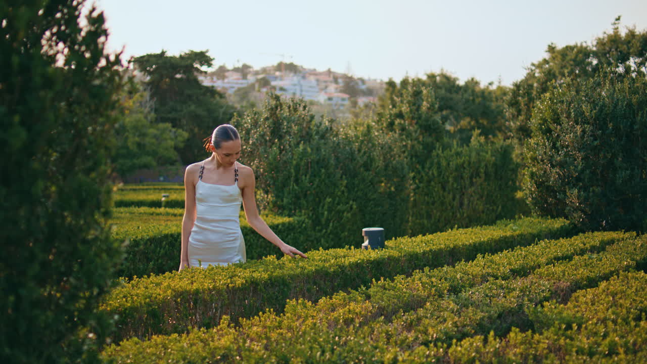 녹색 공원에서 덤불을 만지는 꿈 같은 여자. 정원에서 서 있는 만적인 소녀