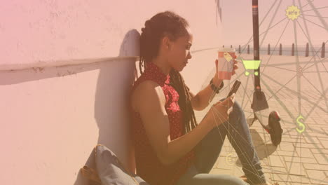 globe of digital icons against african american woman using smartphone sitting on the promenade