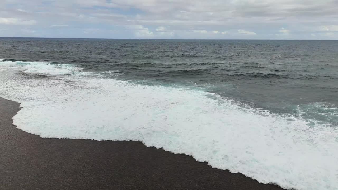 Static aerial shot of ocean waves breaking over the reef surrounding Magpupungko Tidal Pool in Siargao Islands, Philippines, with foamy water patterns under a bright tropical sky