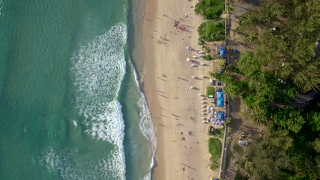 Vertical-view-on-the-coast-of-Phuket-Island,-Thailand,-with-a-beautiful-beach,-turquoise-water-and-waves-reaching-the-shore