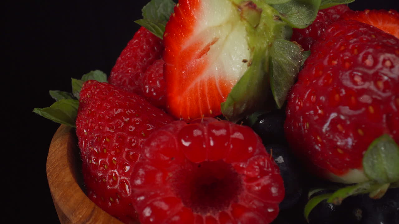 Delicious rotating forest berries in a wooden bowl, wet bright fruits, strawberries, blueberries, raspberries, 4K macro shot