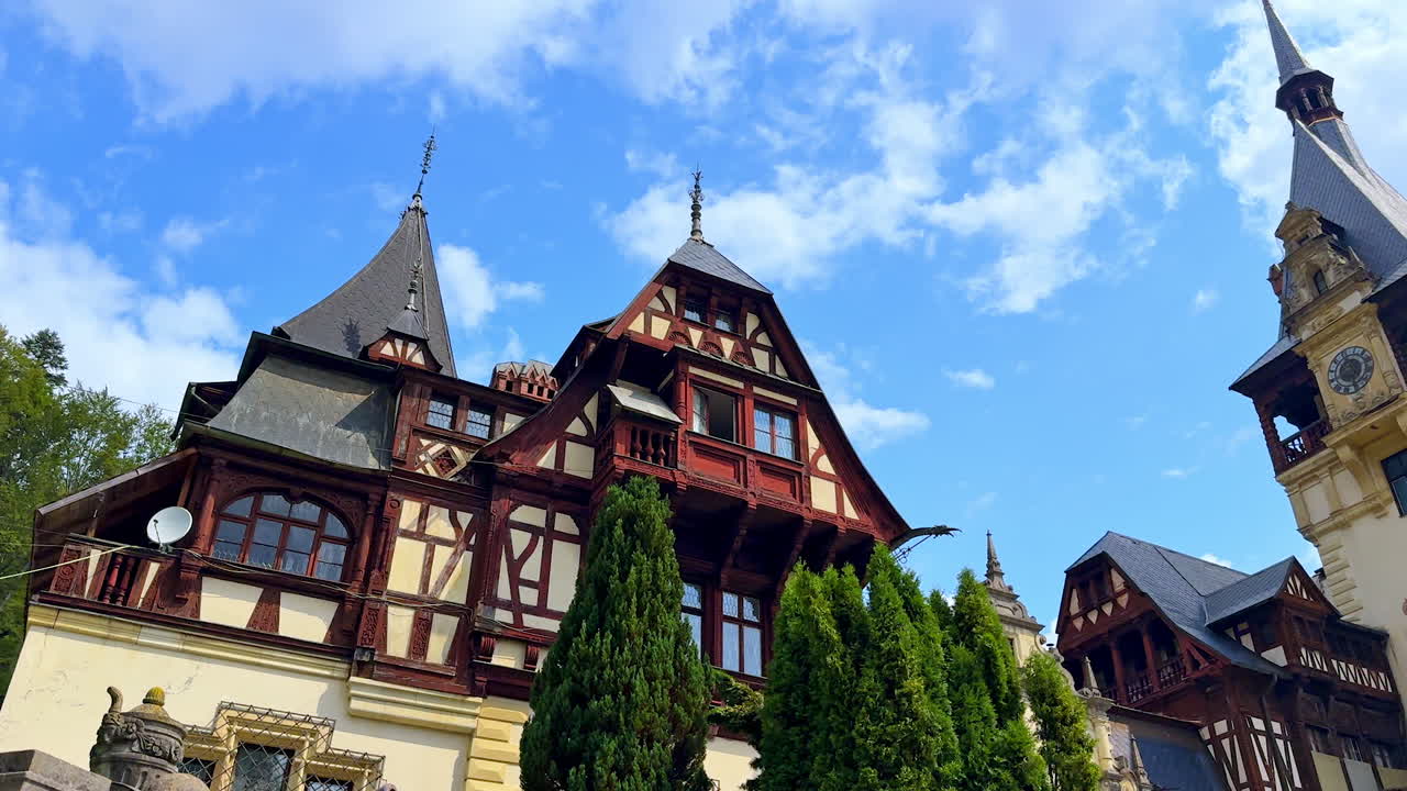 Roofs with tiles and steeples of the Peles Castle in Sinaia, the Carpathians, Romania. Low angle view. Blue sky with white clouds at backdrop