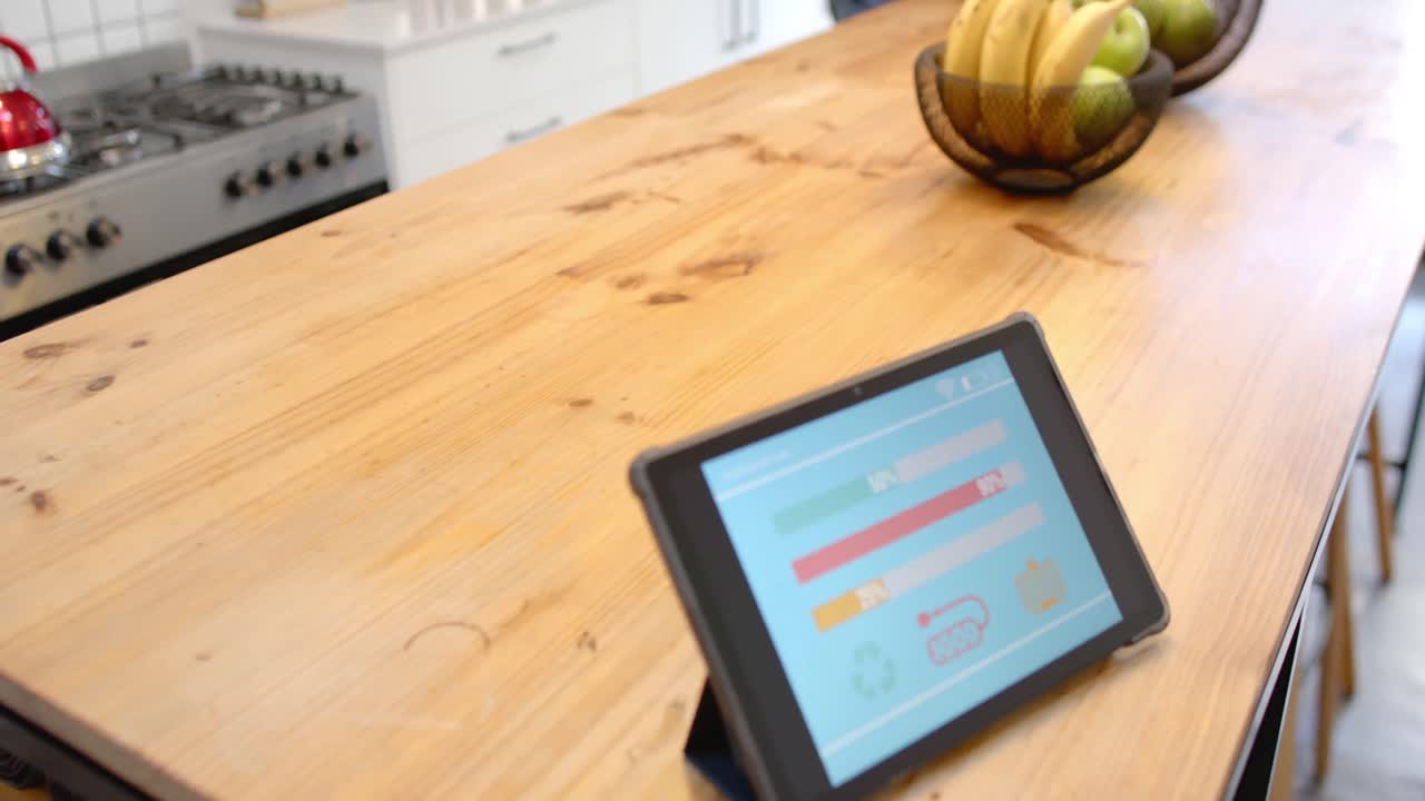 Tablet with smart home interface on wooden table in kitchen, slow motion