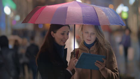 amigas usando el touchpad en una noche lluviosa en la ciudad