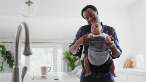 Father-With-Baby-Son-In-Sling-Multi-tasking-Working-From-Home-On-Laptop