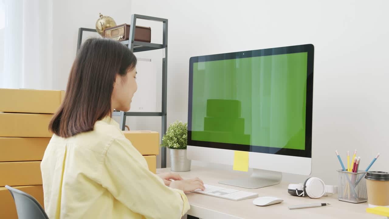 pequeña empresa de puesta en marcha, joven mujer asiática comprobando el pedido en línea en la computadora con pantalla verde. y embalaje de cajas para productos para enviar a los clientes.
