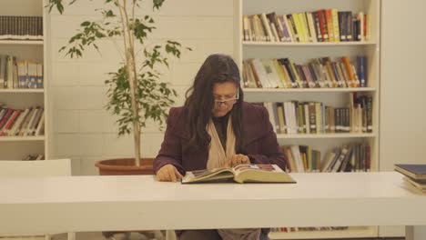 Mujer-Madura-Leyendo-Un-Gran-Libro-En-La-Biblioteca.-Mano