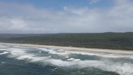 Olas-Espumosas-En-La-Playa-Principal-Con-Un-Vasto-Bosque-En-El-Punto-De-Observación,-Qld-Australia