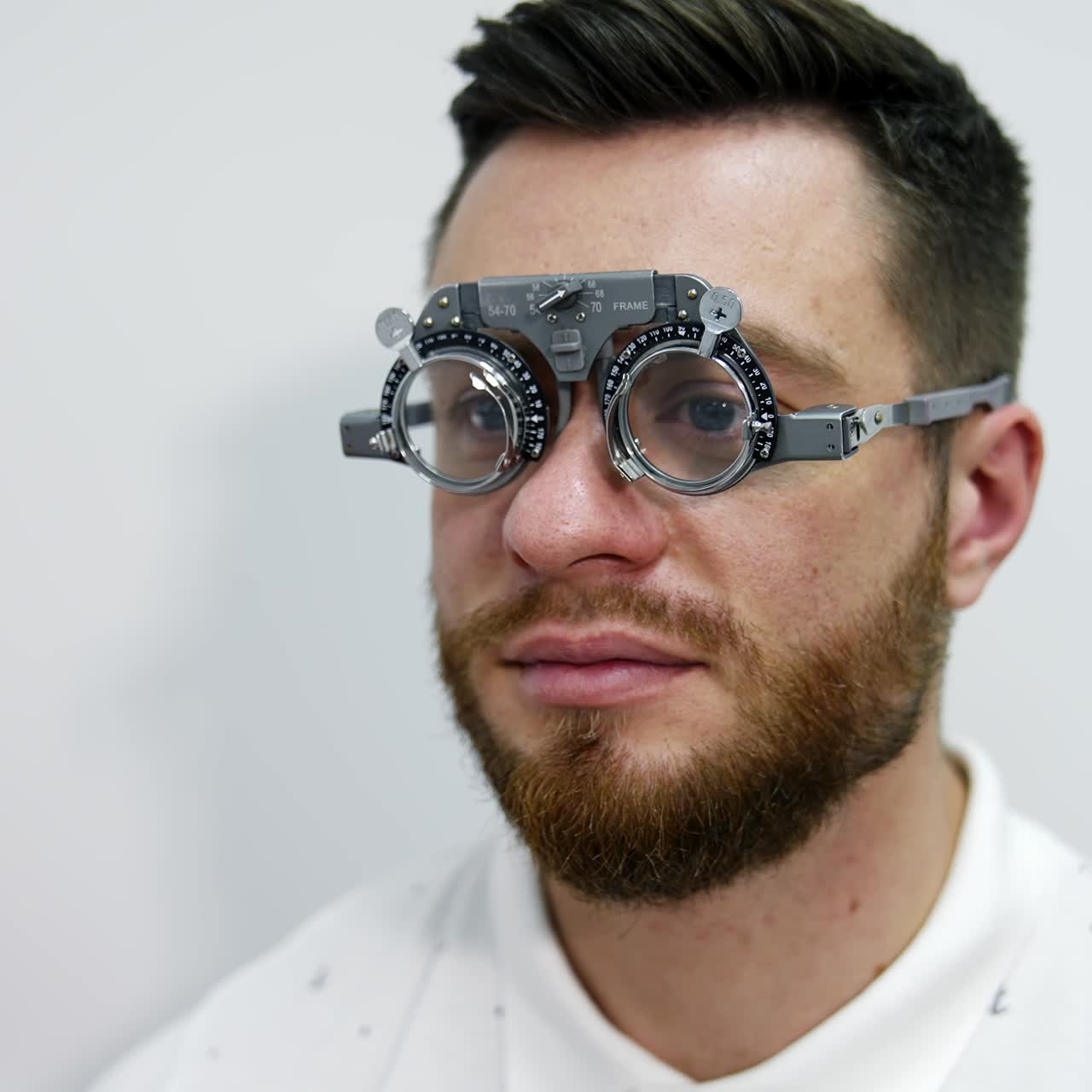 Face of a man in trial frame on eyes. Patient examining his eyesight with a special testing glasses in clinic. Doctor puts lenses into the trial frame. Ophthalmology