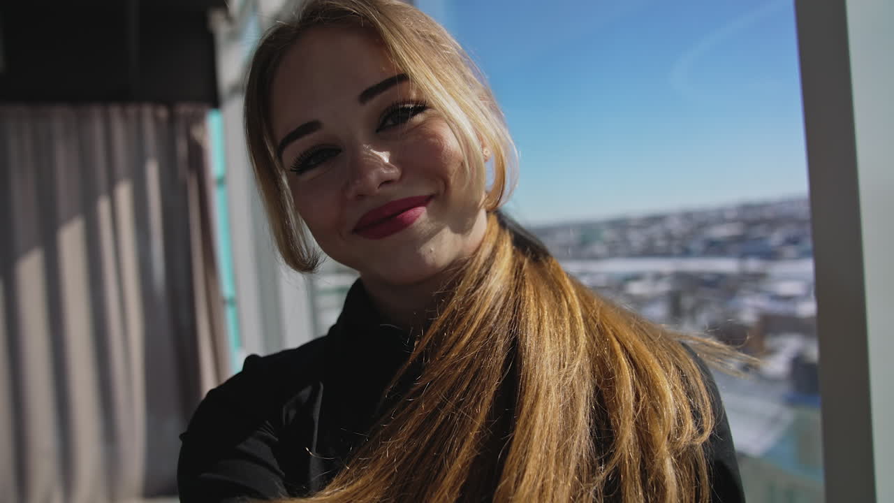 Smiling red-haired young adult lady takes selfie. Big-eyed pretty woman steps back before the camera. Close up.