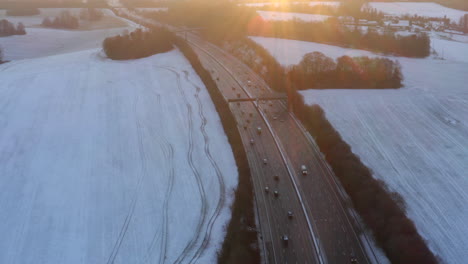 Drohnenaufnahmen-Von-Der-Autobahn,-Umgeben-Von-Schnee-Auf-Feldern,-Mit-Autos,-Die-Morgens-Zum-Sonnenaufgang-Auf-Der-M25-Fahren