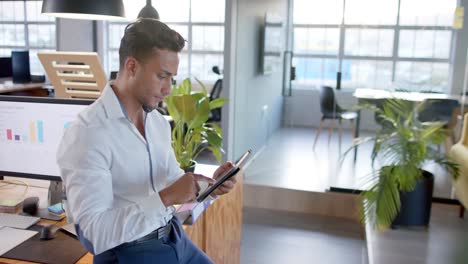 Portrait-of-happy-smart-casual-biracial-businessman-using-tablet-in-office,-smiling,-in-slow-motion