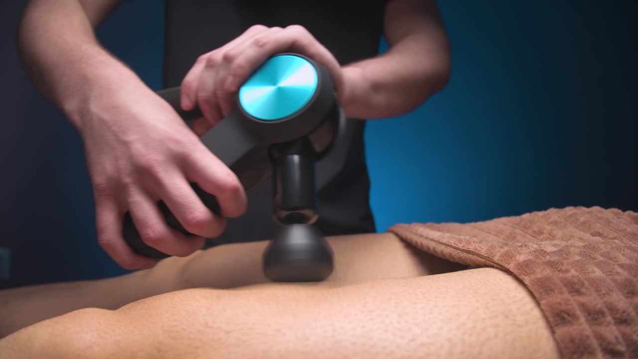 남성 마사지 (massage) 는 남성 클라이언트에게 타악기 비브로 마사지의 도움으로 허지에 마사지 운동을 수행합니다. 운동체의 재생 마사지를 위한 충격 치료.