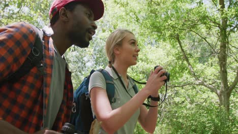 Happy-diverse-couple-with-backpacks-taking-photos-in-park,-slow-motion