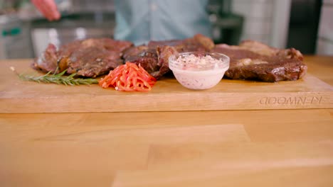 hombre con un bistec de ternera marinado a la parrilla sobre una tabla de madera colocada sobre la mesa lista para servir