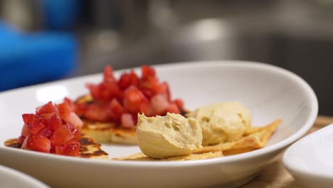 Aperitivo-Saludable-De-Hummus-En-Chips-De-Pan-De-Pita-Con-Tomates-Cortados-En-Cubitos-Servidos-En-Un-Plato-Blanco-O-Tazón-En-Una-Mesa-De-Madera,-Comida-Cerrada