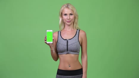 young happy beautiful woman showing phone and giving thumbs up ready for gym