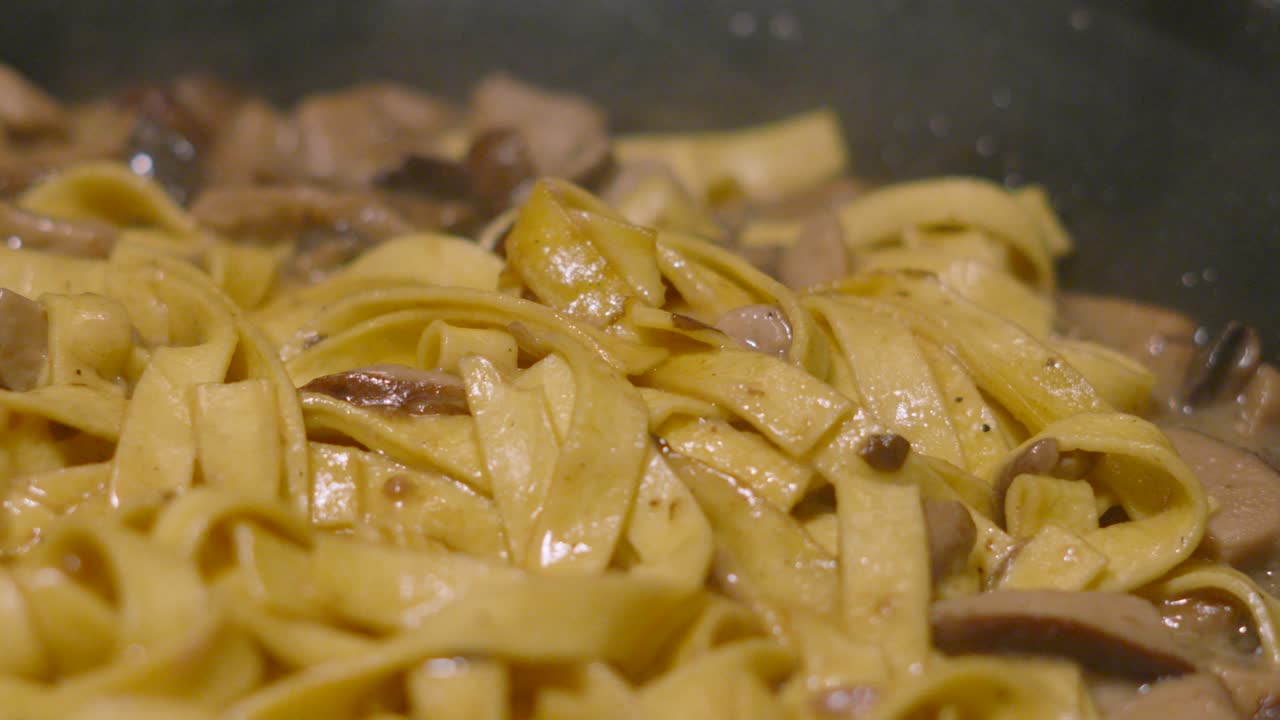 Slow Pan Close Up Details of Italian Mushroom Tagliatelle Being Cooked Gently in Hot Pan with Various Fungi Including Champignon, Shitake, Nameko. Home Cooked Cream Sauce Based Pasta Dish.