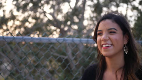 beautiful young hispanic woman looking happy and laughing at a funny conversation with a friend in the park at sunset