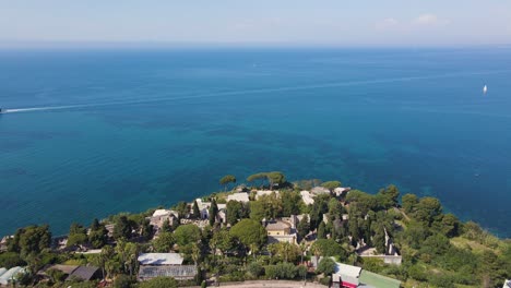 wide angle drone shot of the beautiful tropical island of ischia with a cruise shit and sailing boats in the distance and cars driving on the island