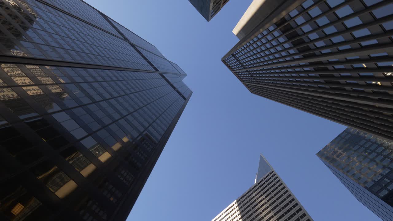 Low angle view of tall skyscrapers in Chicago, showcasing the reflective glass facades of buildings under clear blue sky, emphasizing the city's modern architectural design