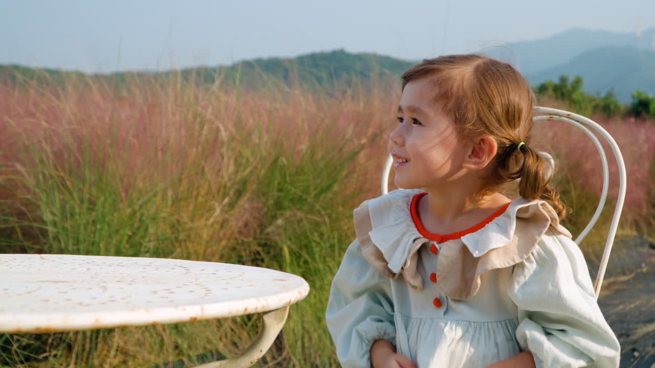 niña pequeña juguetona aplaudiendo en la mesa durante un picnic por la hierba rosa muhly o muhlenbergia capillaris
