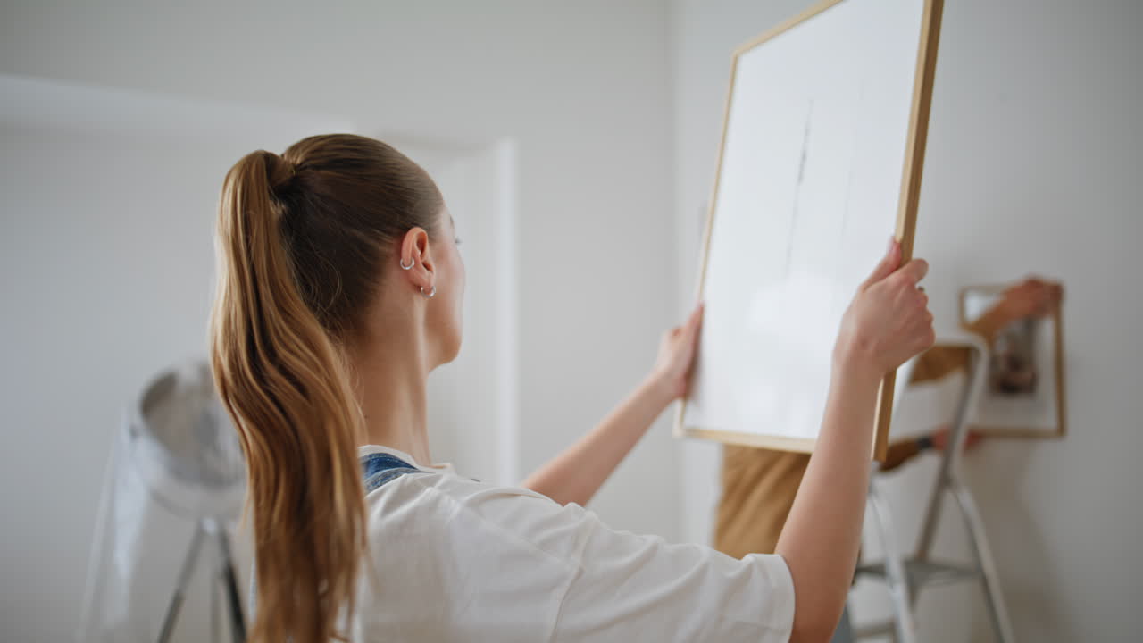 Woman examining framed picture in bright room closeup. Loving couple decorating