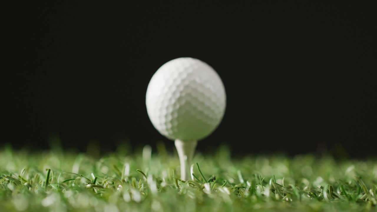Close-up van golftee en bal op gras en zwarte achtergrond, met ruimte voor tekst, in slow motion.