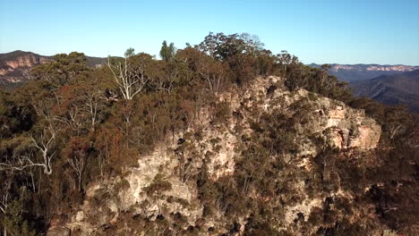 Aerial:-Drone-rising-high-over-a-mountain-reveal-a-beautiful-blue-lake-surrounded-by-mountains-in-New-South-Wales,-Australia