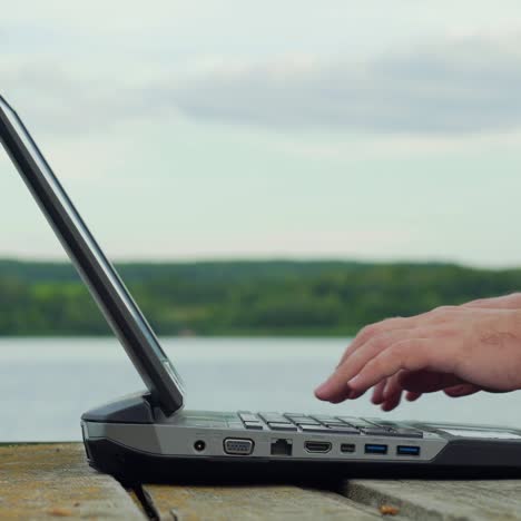 Man's hands using laptop computer. Young man using laptop on the pier.