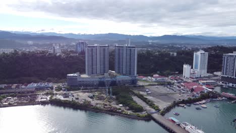 drone flies away from apartment building revealing small harbours and neighbouring ships in the scenic morning of kota kinabalu, malaysia