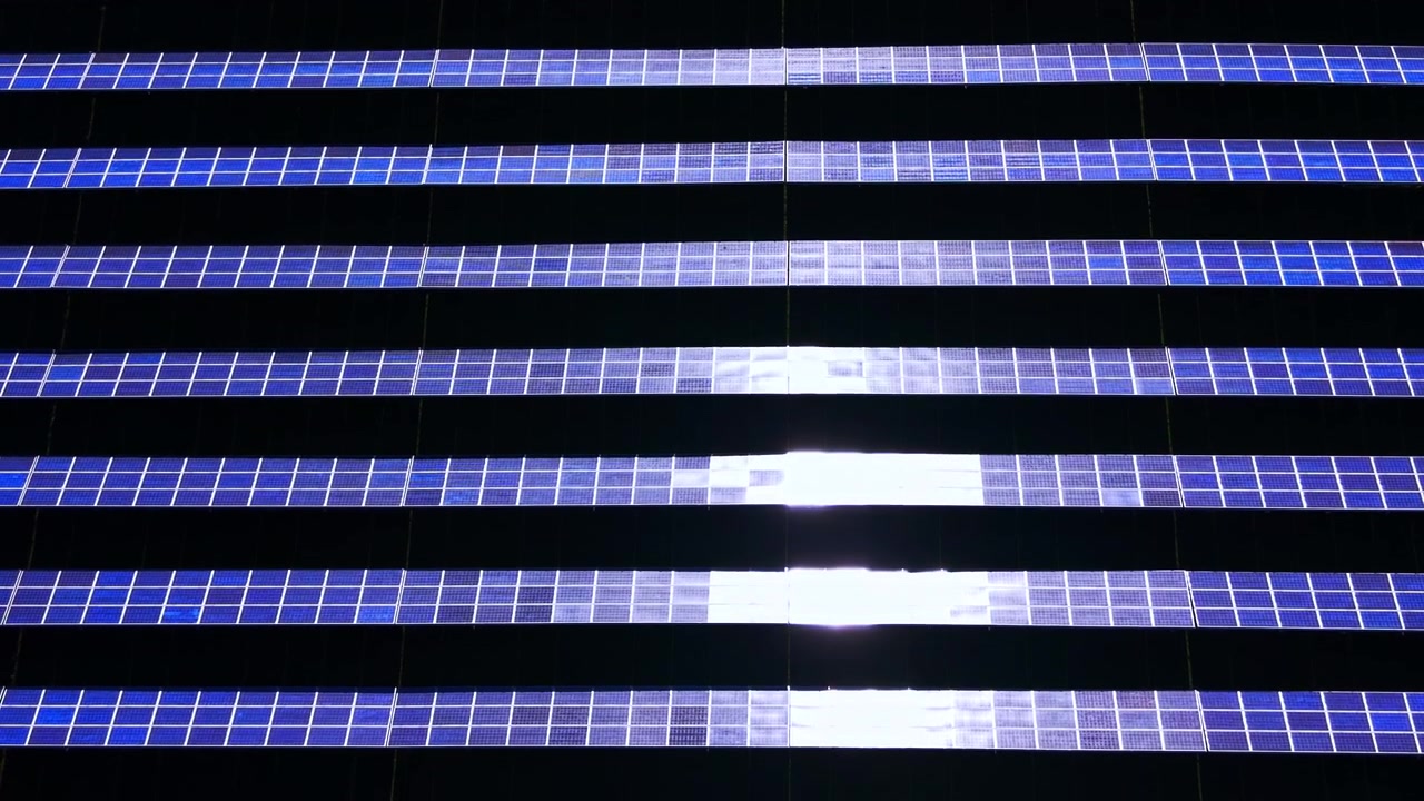 Symmetric overhead perspective of alternative energy array with central sun glint reflection on blue modules. Horizontal rows of solar panels at photovoltaic farm.