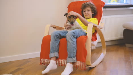 Blond-Boy-Sitting-On-The-Chair-While-Swinging-With-His-Dog-And-Caresses-Him