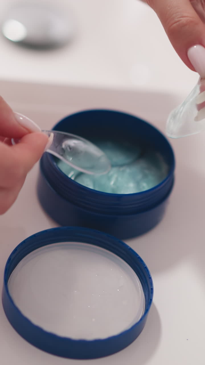 mano de mujer toma parche cosmético para la piel de los ojos usando espátula cosmética. mano toma parche ocular con espátula de frasco de plástico de pie en la mesa de luz