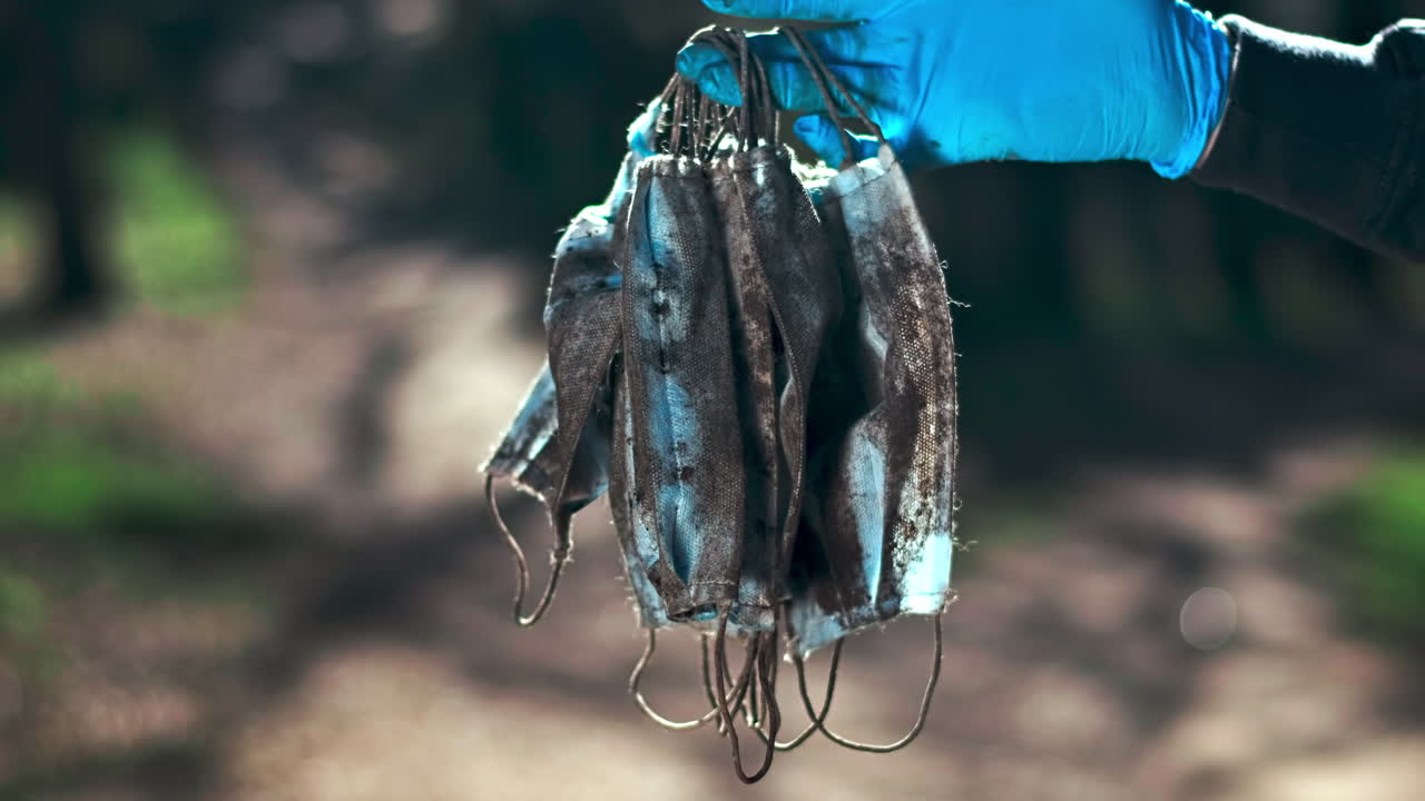Man in medical gloves holding a bunch of dirty medical masks raised from the ground. Pollution idea