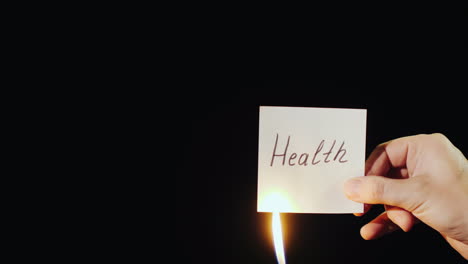 hand holds burning paper with inscription health