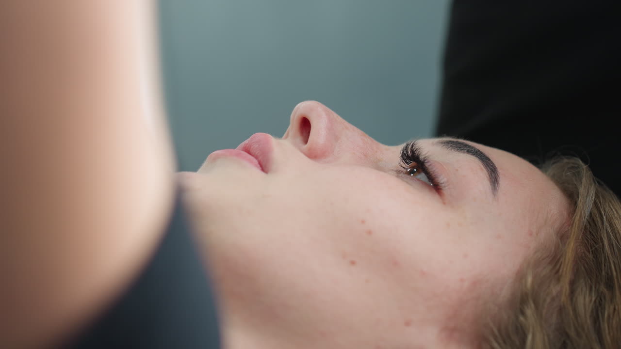 close up of young woman lying on bench with calm focused expression, likely engaged in workout session, showing natural facial details and soft lighting in modern gym setting with neutral background