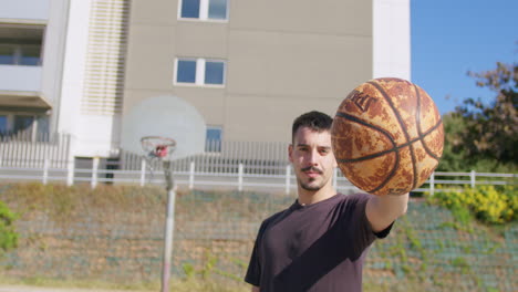 tiro medio en cámara lenta de un joven caucásico sosteniendo una pelota y mirando a la cámara en una cancha de baloncesto de la calle