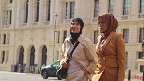 two muslim businesswomen wearing hijabs with modern business suits walking to work past city office buildings 1