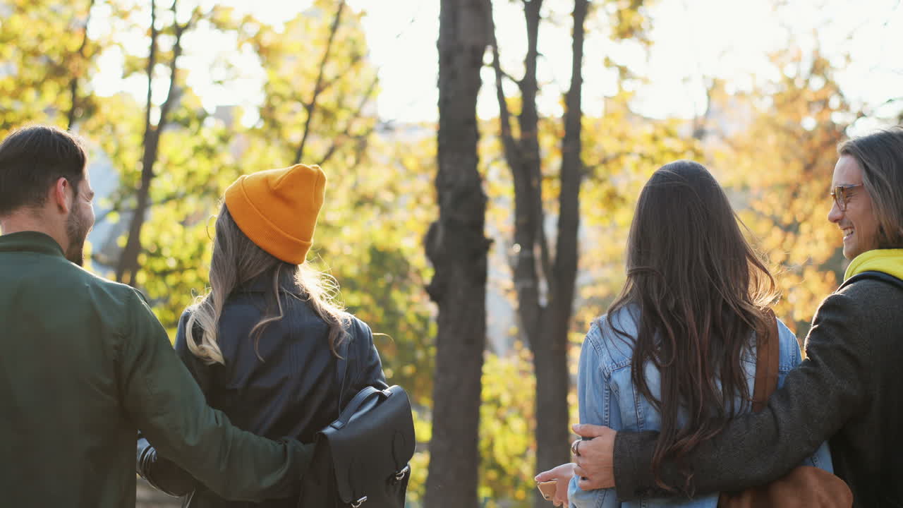 vista trasera de un grupo de amigos caminando y abrazándose en el parque en otoño