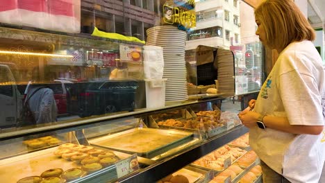 a woman selects egg tarts from a bakery