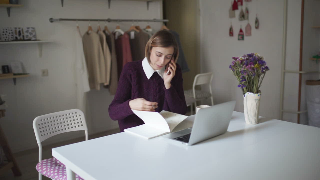 mujer joven sentada a la mesa y hablando por teléfono móvil. mujer usando computadora portátil